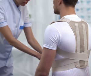 Orthopedist applying posture control shoulder brace male patient, healthcare